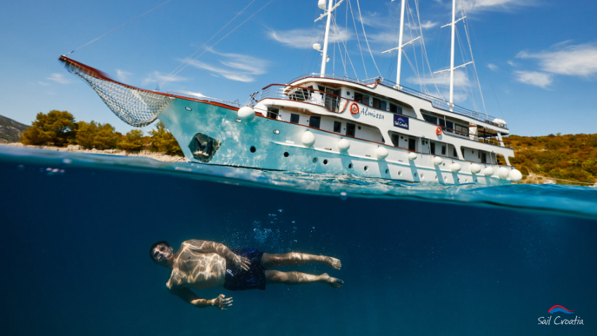 A young adult swimming beneath a traditional Croatian ship on a Sail Croatia tour.