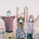 Three Topdeck travellers standing on a bench with a European city in the background all wearing face masks.