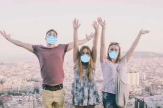 Three Topdeck travellers standing on a bench with a European city in the background all wearing face masks.