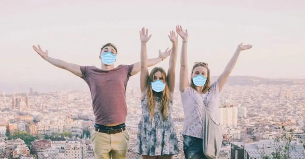 Three Topdeck travellers standing on a bench with a European city in the background all wearing face masks.