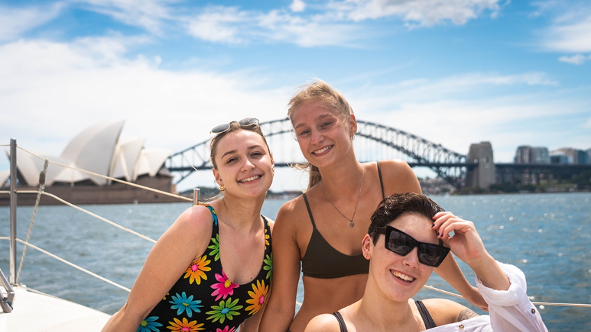 Three young working holiday makers on a boat in front of the Sydney Harbour Bridge