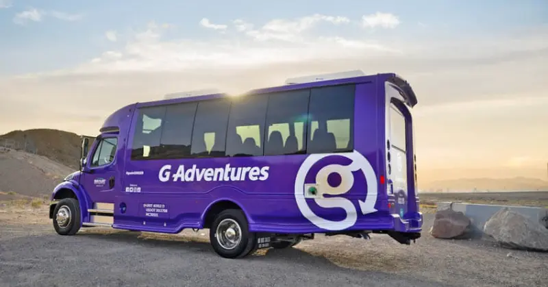 The distinctive purple G Adventures tour bus parked in a scenic desert landscape at dusk.