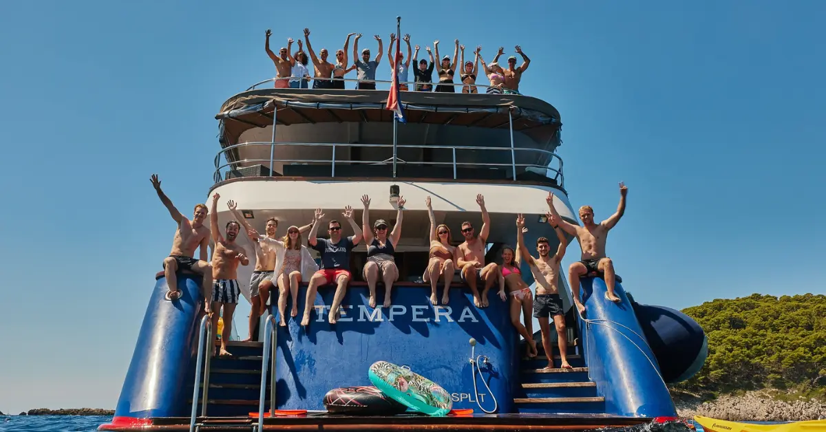 Joyful young adults with raised hands on the back of the 'Tempera', a Sail Croatia Navigator cruise ship.