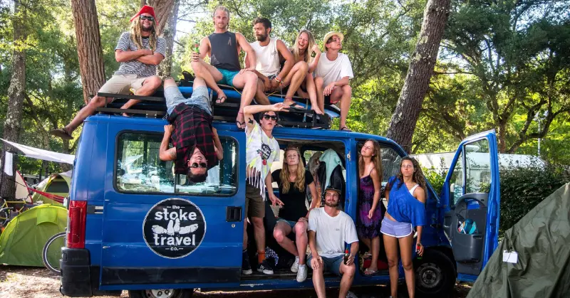 A group of young, lively travellers posed on and around a Stoke Travel van, ready for wild festivals and parties.