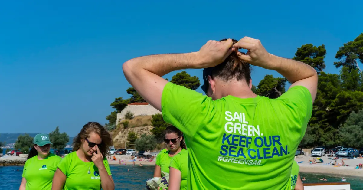 People on a beach wearing bright green shirts with the Green Sail branding on the back