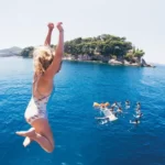 A young woman jumping off a boat into the Adriatic Sea with a group of others swimming near by