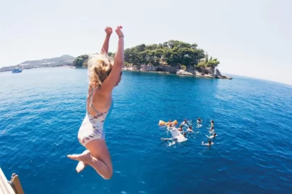 A young woman jumping off a boat into the Adriatic Sea with a group of others swimming near by