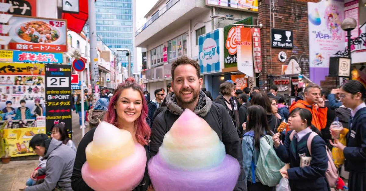 A cheerful couple holds giant, colourful cotton candy on a bustling street in Japan.