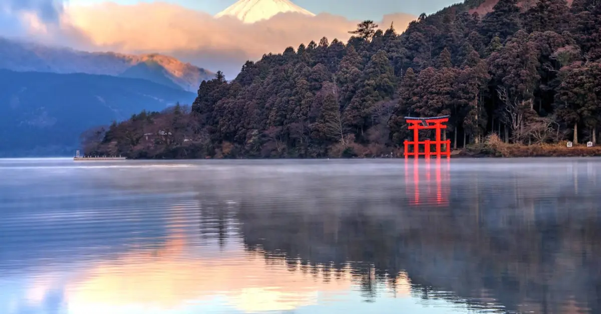 Serene Lake Ashi with a vibrant red torii gate, reflecting the calm waters with Mount Fuji in the background.