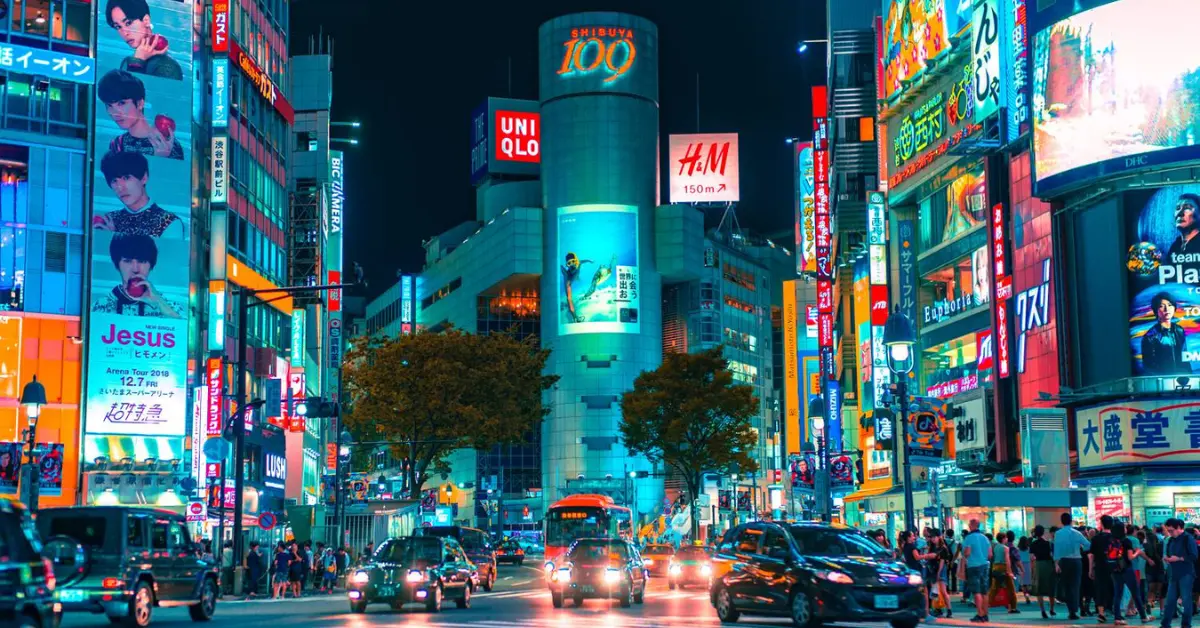 Bustling Shibuya Crossing in Tokyo at night, illuminated by neon signs and busy with traffic.