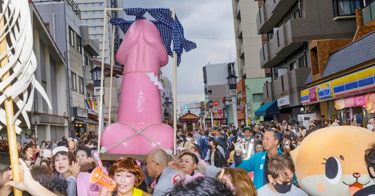 A crowd at the Kanamara Matsuri in Japan with a large pink phallic-shaped sculpture.