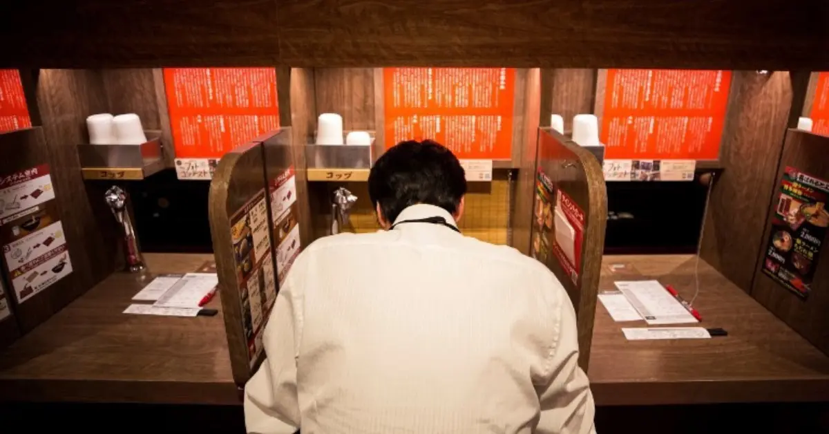 A man in a white shirt studying a menu. Dining solo is a common practice in Japan.