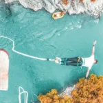 A young adult bungee jumping over a clear turquoise river from a wooden platform, depicting the thrill-seeking activities often considered when purchasing travel insurance for under 35s