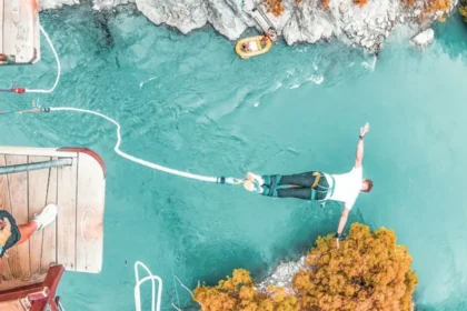 A young adult bungee jumping over a clear turquoise river from a wooden platform, depicting the thrill-seeking activities often considered when purchasing travel insurance for under 35s