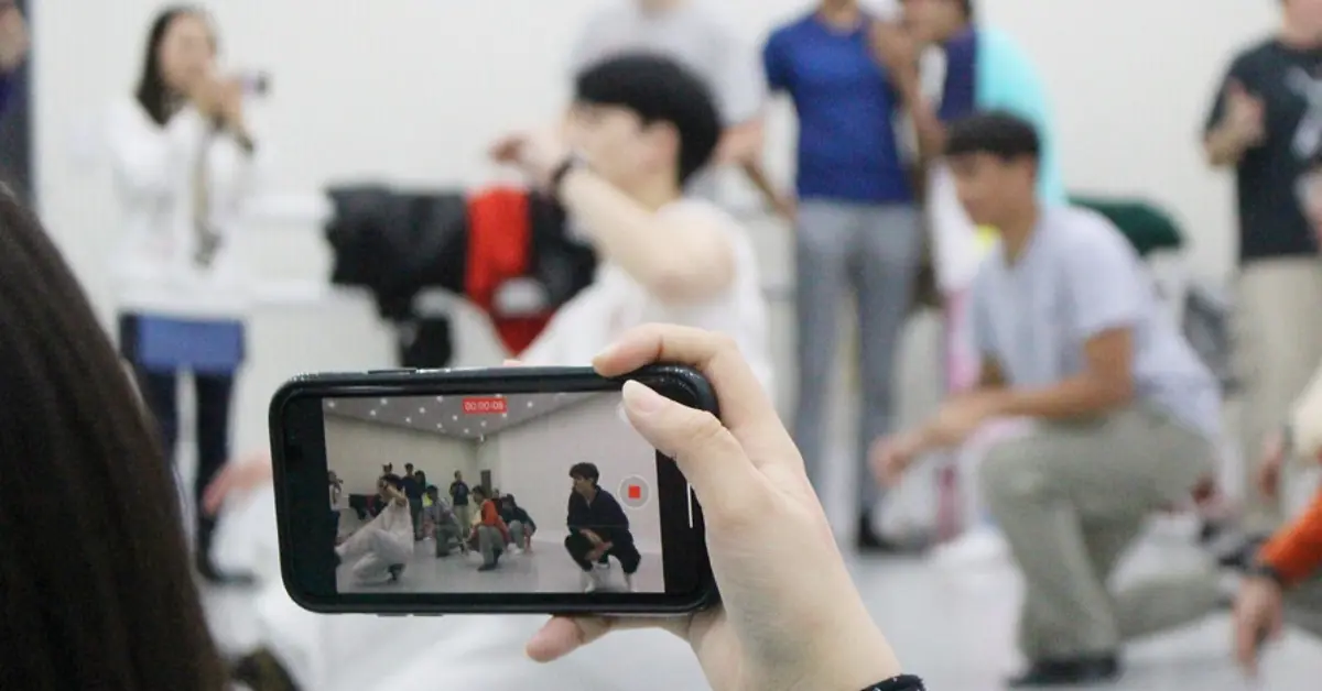 A person capturing a K-pop dance session on their smartphone, with a professional instructor leading a group in a dance studio, as part of a One Life Adventures tour experience.