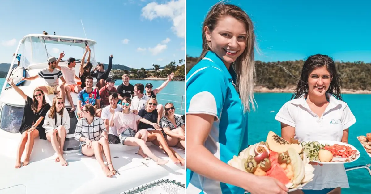 A group of young adults enjoying their time on a boat in the Whitsundays, with some posing for a photo on the deck and others serving fresh fruit platters, illustrating the vibrant and fulfilling work environment in this beautiful location.